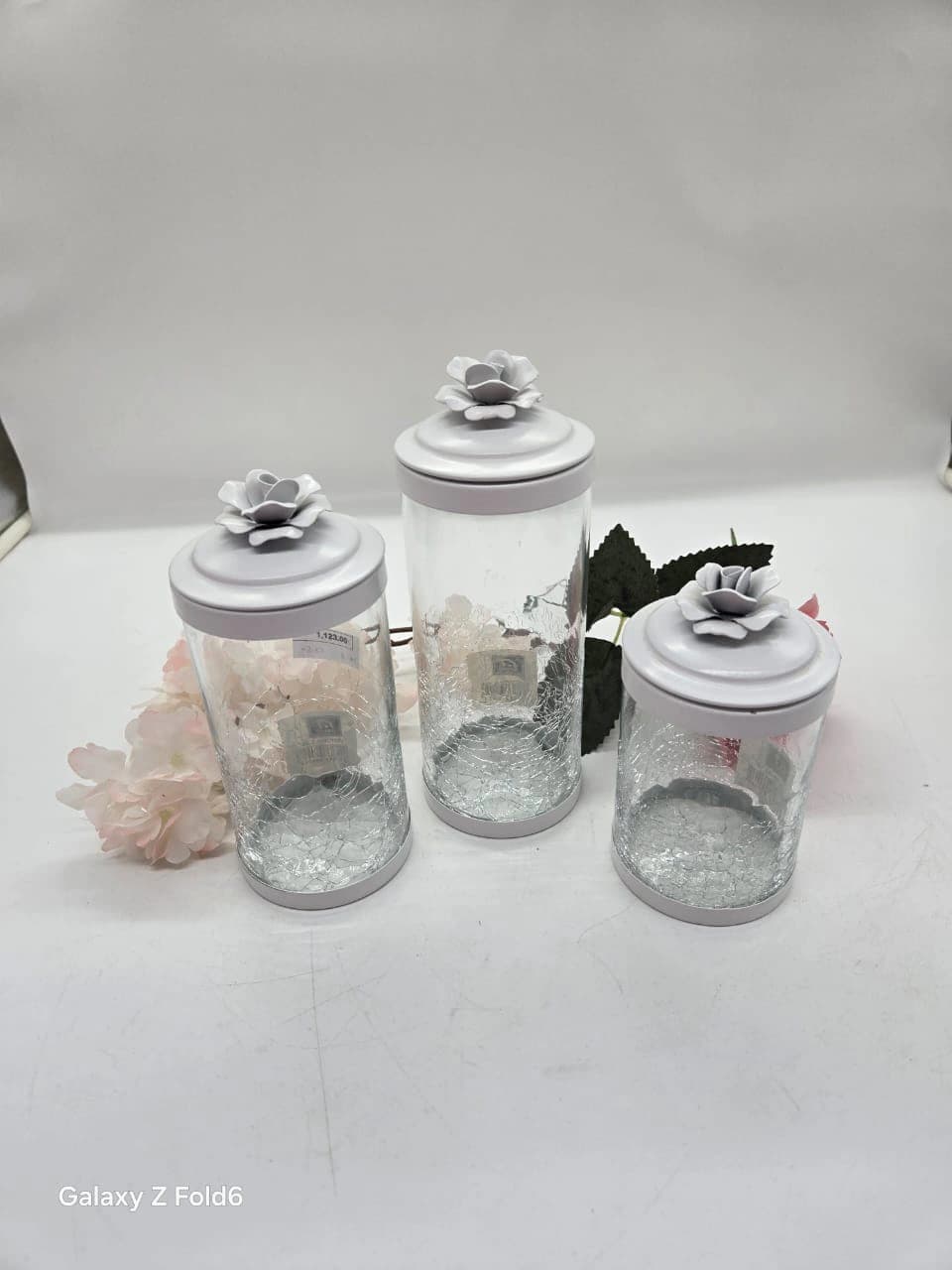 Ensemble de trois bocaux décoratifs en verre à bases craquelées, couvercles surmontés de fleurs blanches