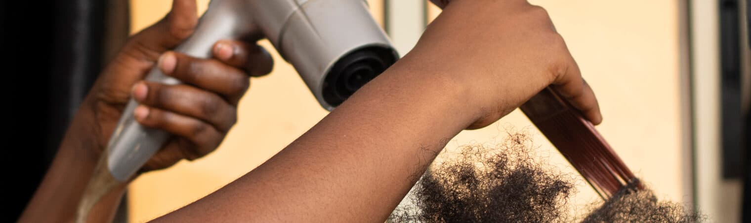 Un brushing en cours au salon : une main tient le sèche-cheveux, l’autre tend une mèche.